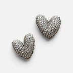 Jakris silver heart-shaped stud earrings covered in sparkling white stones on a white surface