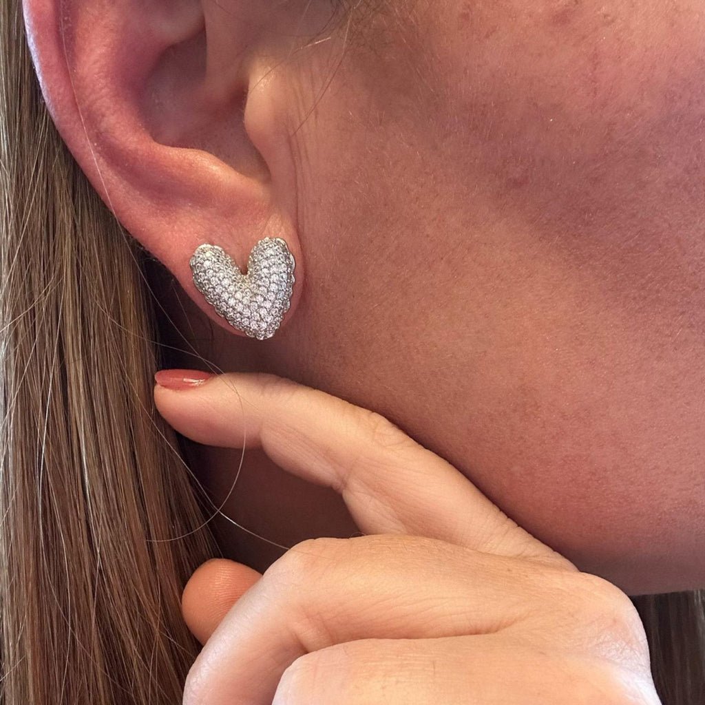 Jakris silver heart-shaped stud earrings covered in sparkling stones worn on a woman's ear