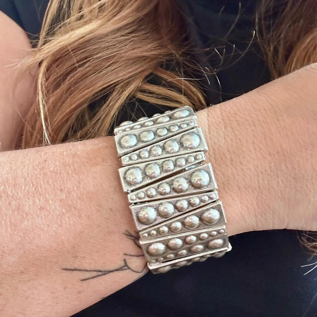 Jakris silver-toned elastic bracelet featuring geometric metal plates with raised stud details on a woman's wrist.