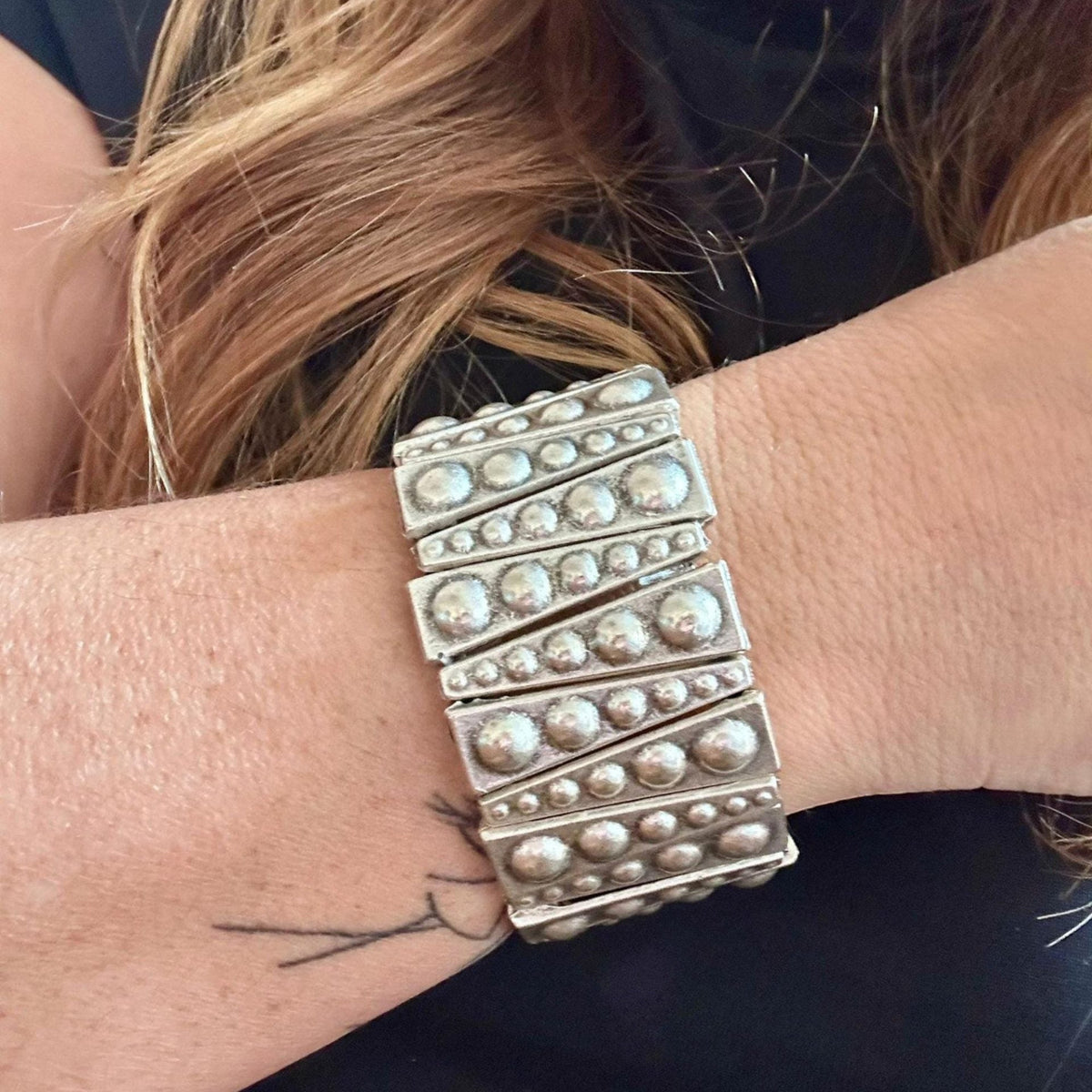 Jakris silver-toned elastic bracelet featuring geometric metal plates with raised stud details on a woman's wrist.
