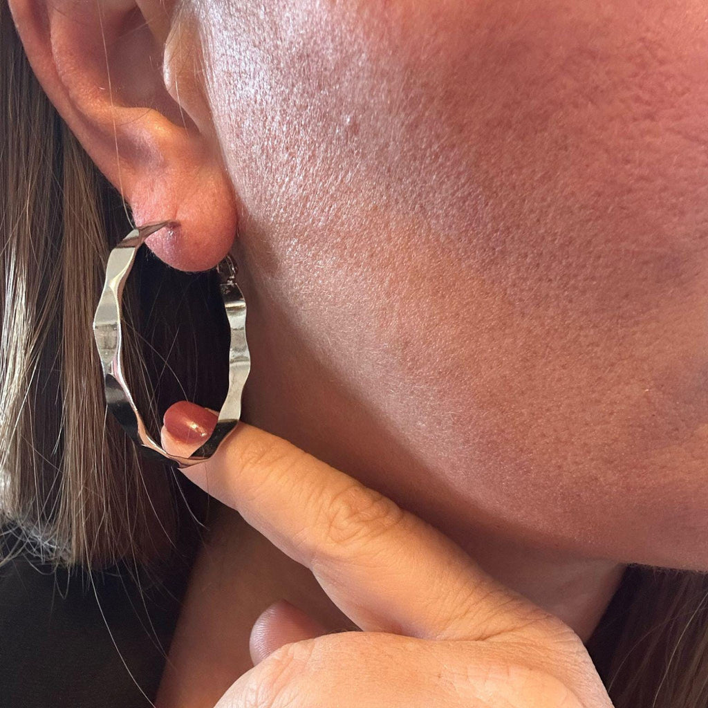 Jakris silver-toned wavy hoop earring worn on a model's ear, featuring a lightweight and modern textured design.