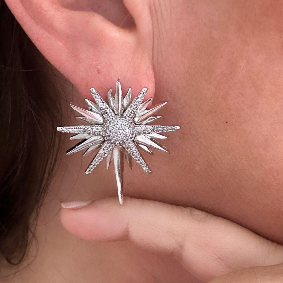 Jakris silver-toned star-shaped earring with sparkling zircon stones worn on an earlobe