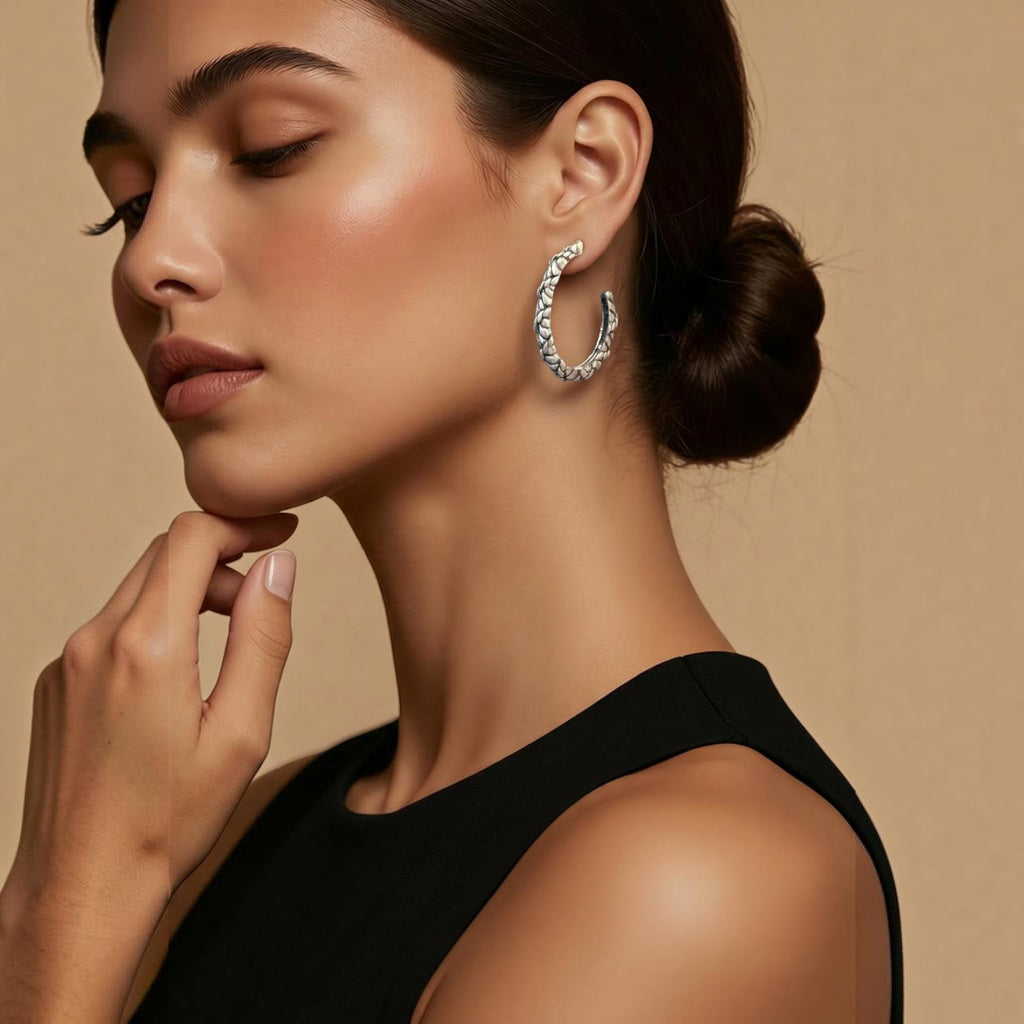 Jakris silver-plated hoop earrings with a textured surface worn by a woman with a sleek bun hairstyle.