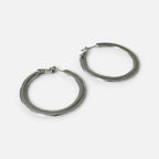 Jakris thick silver hoop earrings with a classic polished finish resting on a soft white fabric background.