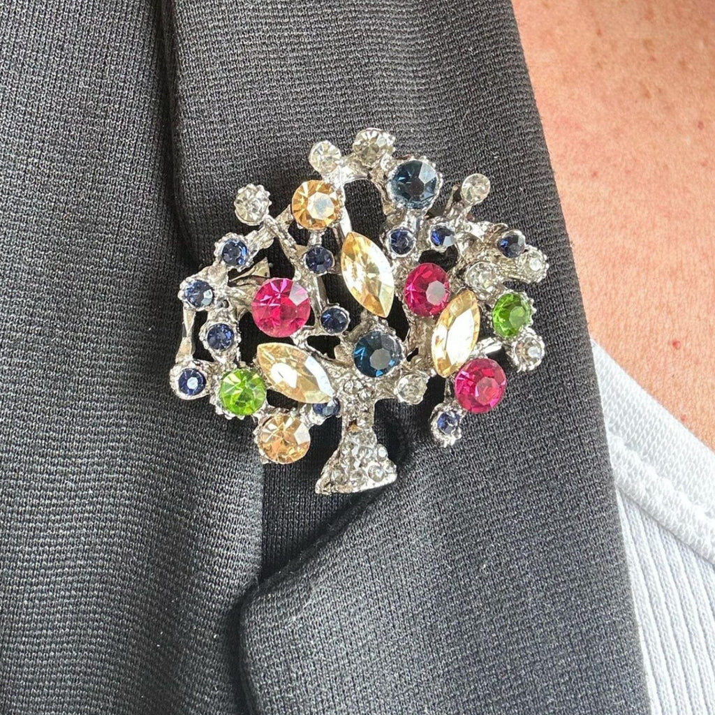 Jakris vintage tree of life brooch featuring colorful crystal stones pinned to a dark grey blazer lapel
