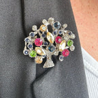 Jakris vintage tree of life brooch featuring colorful crystal stones pinned to a dark grey blazer lapel