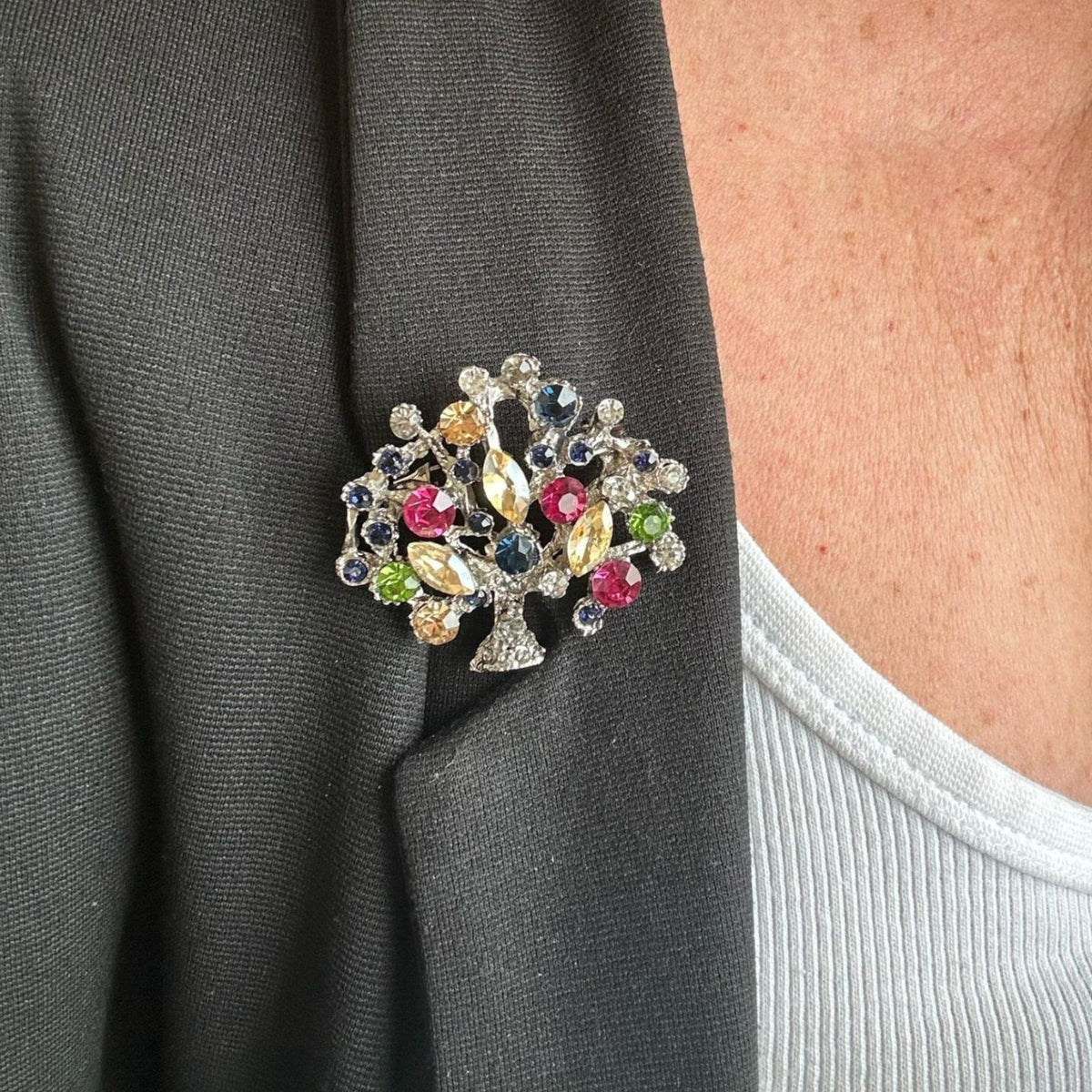 Jakris vintage tree of life brooch featuring colorful crystal stones pinned on a black blazer lapel
