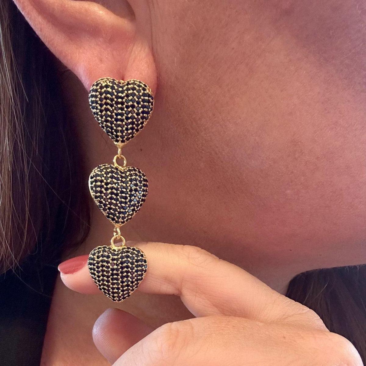 Jakris triple heart drop earrings featuring dark blue pavé stones in a gold setting worn on an earlobe