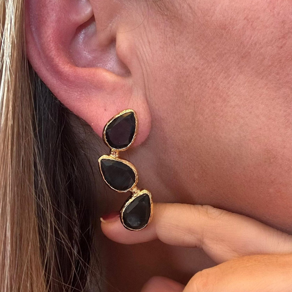 Jakris gold-plated triple teardrop earrings featuring black stones worn on an earlobe