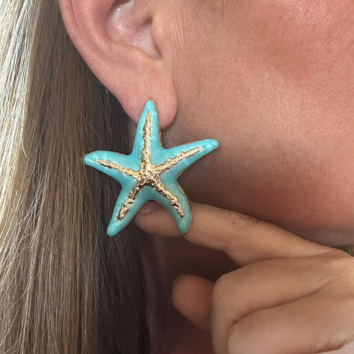 Jakris large turquoise and white starfish enamel earrings worn on an ear for a summer beach style look