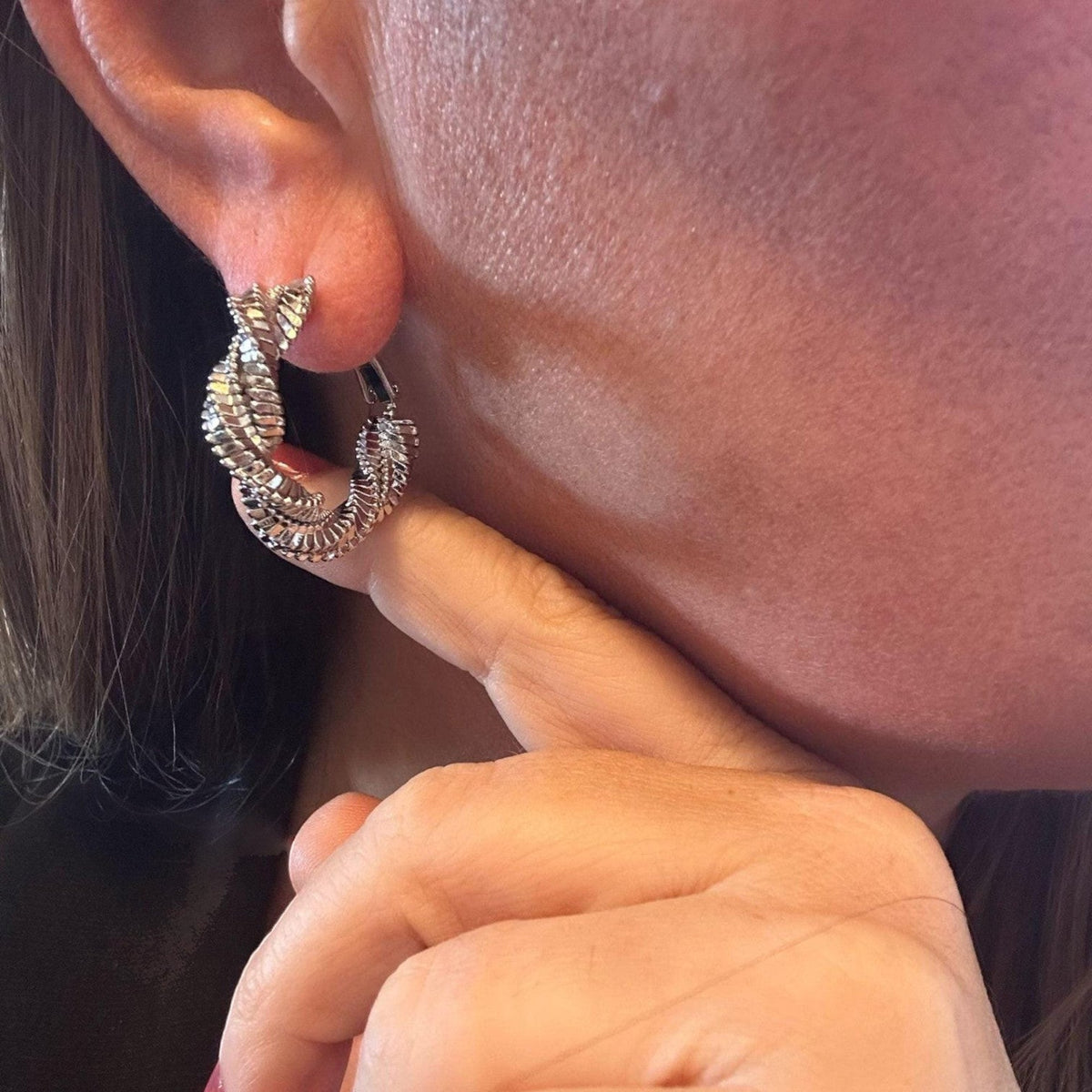 Jakris shiny silver-tone hoop earrings with a twisted textured design worn on an earlobe