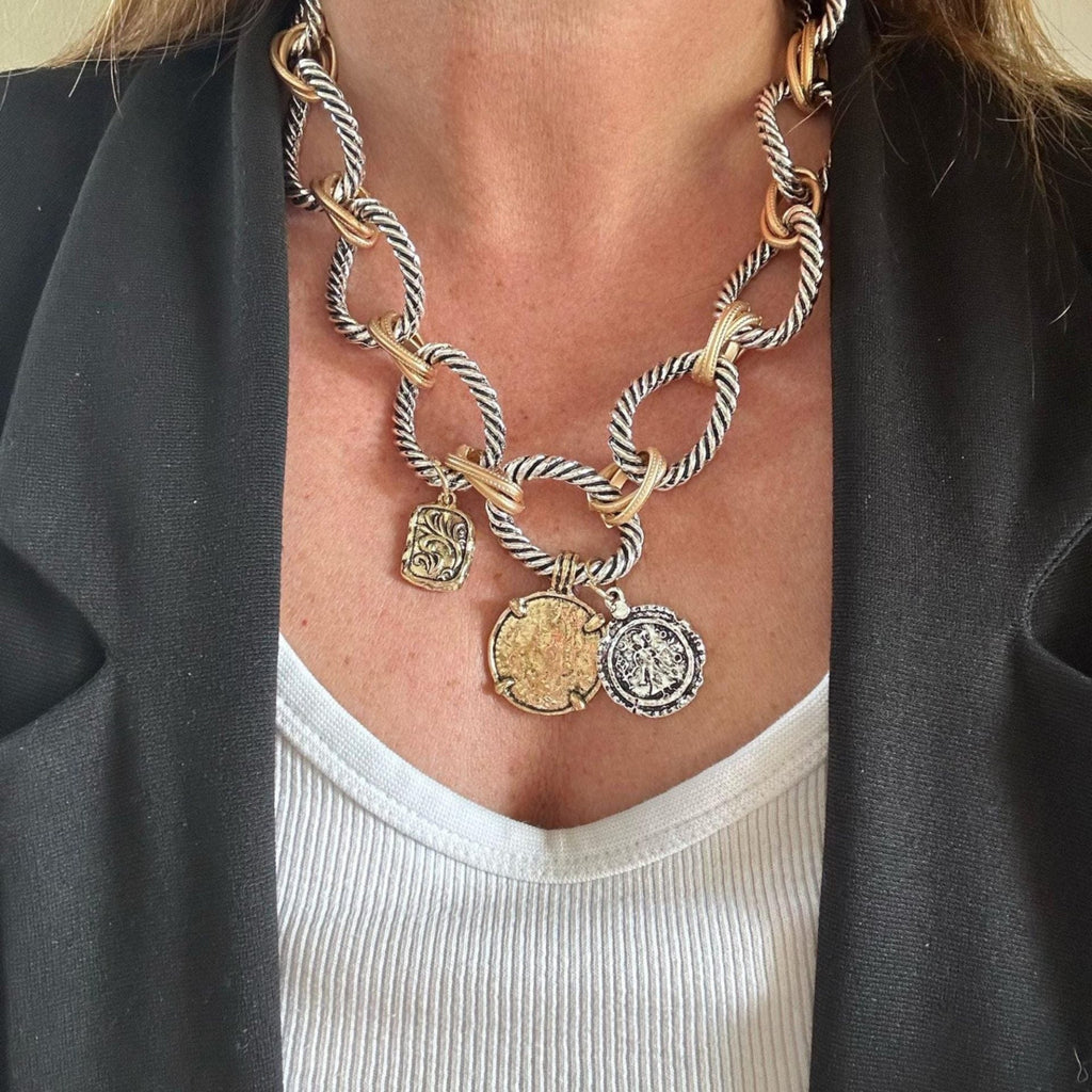 Jakris two-tone chunky chain necklace featuring vintage-style coin charms worn over a white top and black blazer