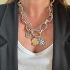 Jakris two-tone chunky chain necklace featuring vintage-style coin charms worn over a white top and black blazer