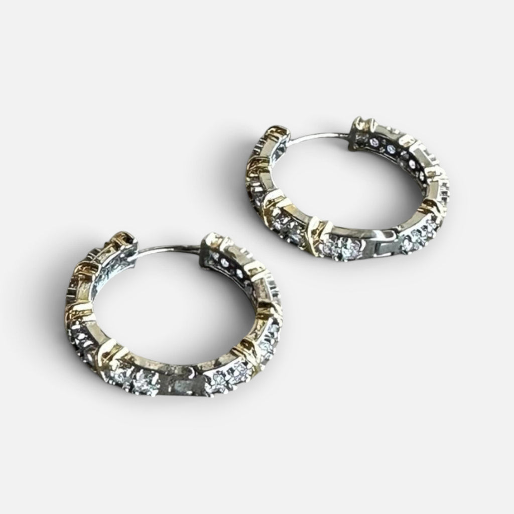 Jakris two-tone hoop earrings in gold and silver featuring sparkling zircon stones on a marble surface.