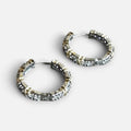 Jakris two-tone hoop earrings in gold and silver featuring sparkling zircon stones on a marble surface.