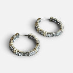 Jakris two-tone hoop earrings in gold and silver featuring sparkling zircon stones on a marble surface.
