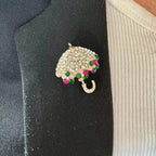Jakris umbrella brooch featuring sparkling clear crystals and colorful gemstone accents pinned to a black blazer
