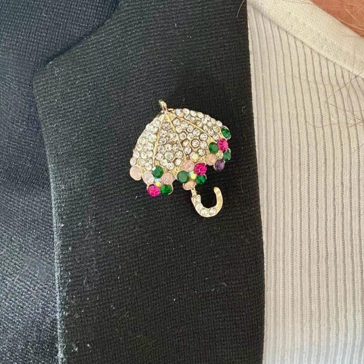 Jakris umbrella brooch featuring sparkling clear crystals and colorful gemstone accents pinned to a black blazer