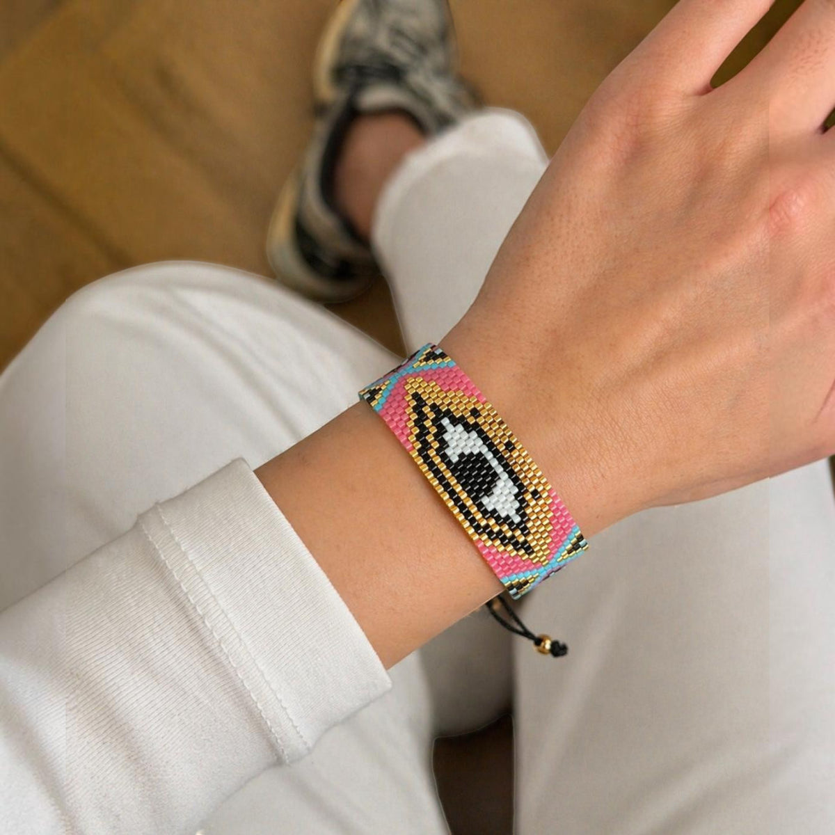 Jakris woven bead bracelet featuring a colorful evil eye pattern in pink, gold, black, and blue on a wrist.