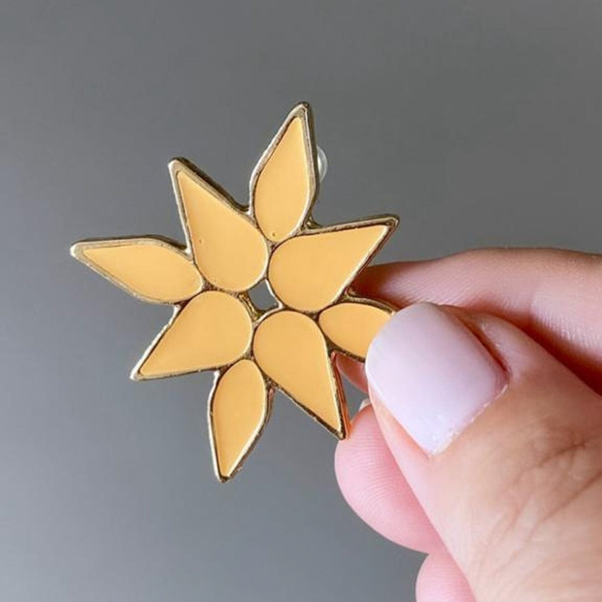 Jakris yellow enamel flower stud earring with gold-tone metal edges held between fingers