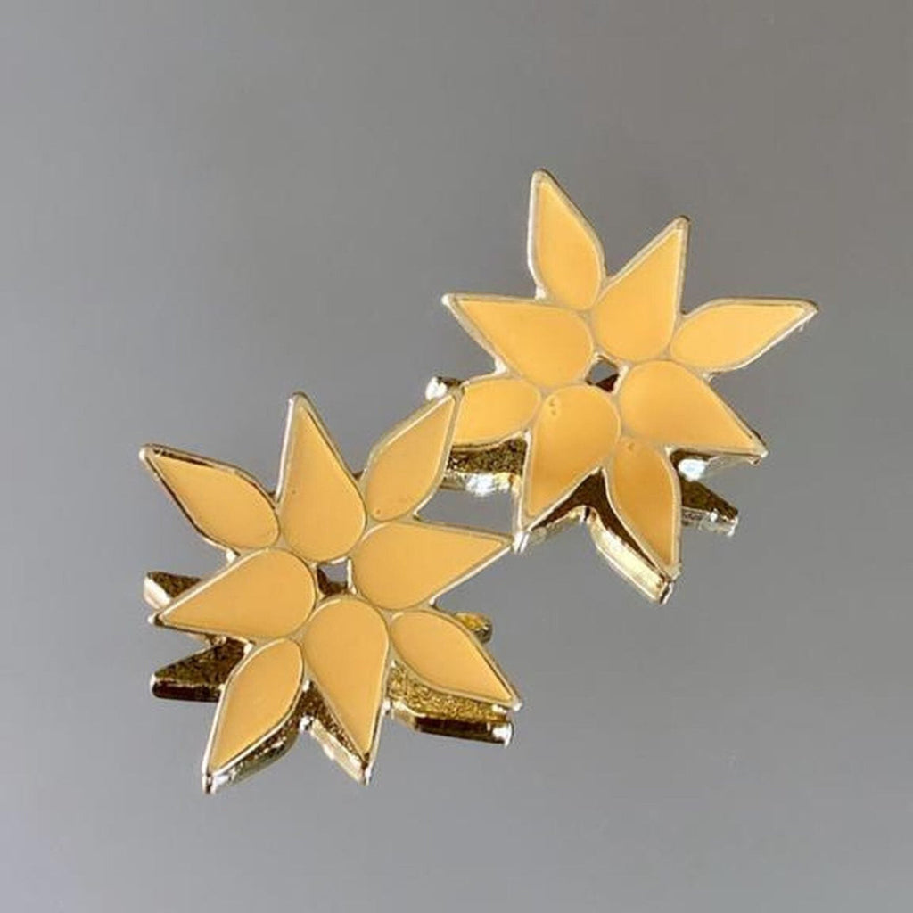 Jakris yellow enamel flower earrings with a star-shaped petal design on a reflective surface.