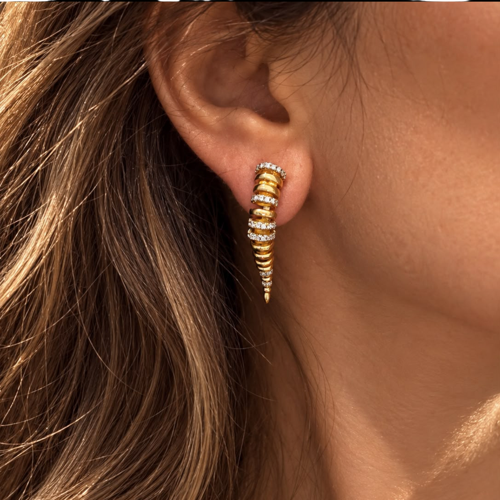 Jakris Zaria gold-plated brass earrings with sculptural curved design and sparkling zircon stone accents on an ear.