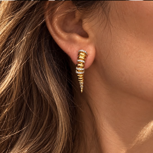 Jakris Zaria gold-plated brass earrings with sculptural curved design and sparkling zircon stone accents on an ear.