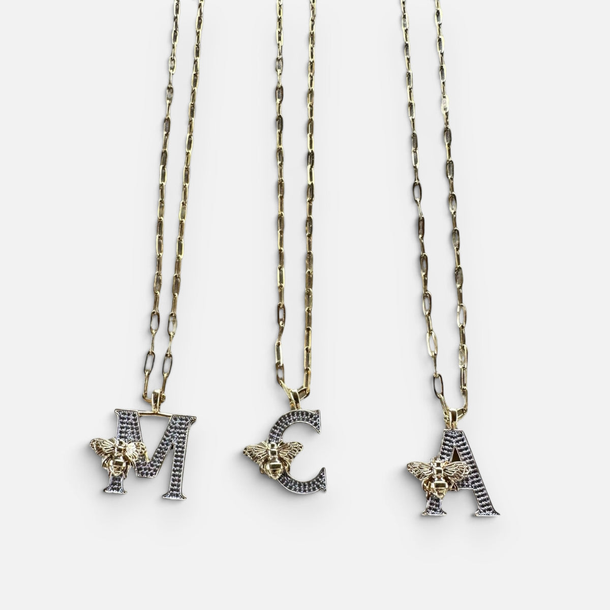 Jakris gold-tone chain necklaces featuring letter pendants M, C, and A adorned with sparkling zircon and bee charms.